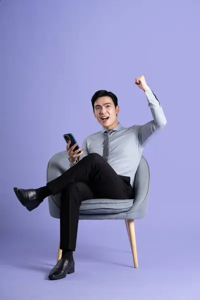 紫色の背景に隔離されたソファに座っているアジアのビジネスマンの肖像画 — ストック写真