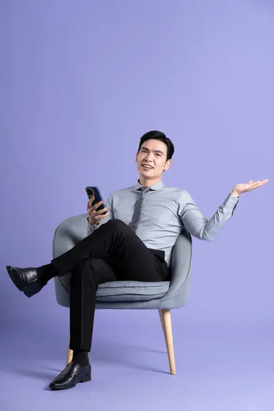 紫色の背景に隔離されたソファに座っているアジアのビジネスマンの肖像画 — ストック写真