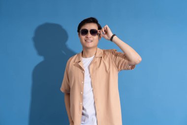 Mavi arka planda poz veren Asyalı bir adamın portresi, yazın seyahat ediyor.