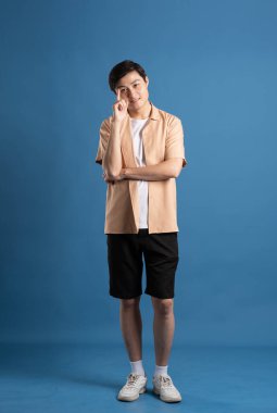 Mavi arka planda poz veren Asyalı bir adamın portresi, yazın seyahat ediyor.