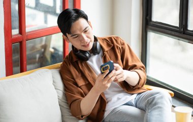 Asyalı bir adamın portresi kafede oturuyor, telefon kullanıyor ve müzik dinliyor.