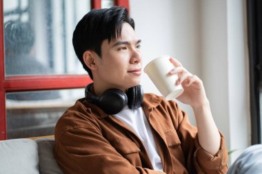 Asyalı bir adamın portresi kafede oturuyor, telefon kullanıyor ve müzik dinliyor.