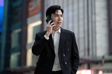 Sokakta, arkasında yüksek binalar olan Asyalı genç bir iş adamının portresi.