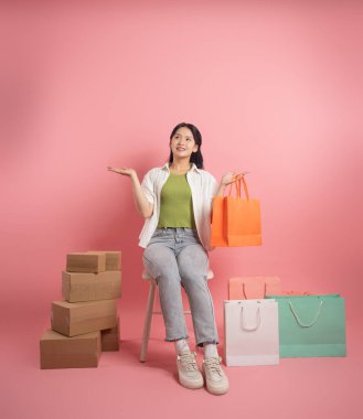 Pembe arka planda, alışveriş torbalarının yanında duran Asyalı kadın portresi.