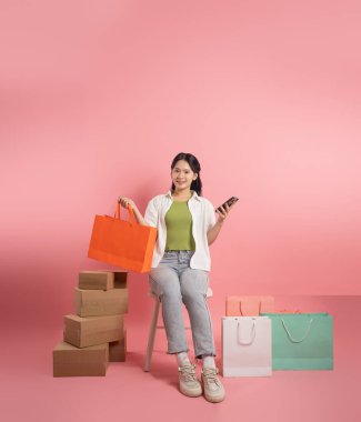 Pembe arka planda, alışveriş torbalarının yanında duran Asyalı kadın portresi.