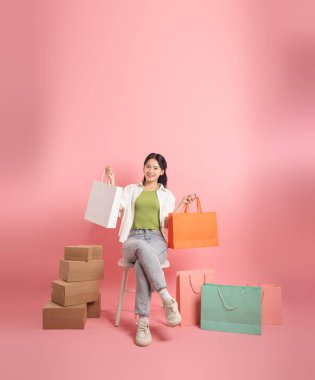 Pembe arka planda, alışveriş torbalarının yanında duran Asyalı kadın portresi.