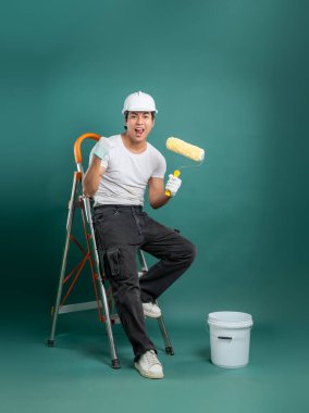 Miğferli ve eldivenli neşeli bir ressam elinde boya silindiri olan bir merdivende oturur. Bir kova boyayla başarıyla bitirilen bir işi kutluyoruz..