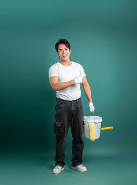 İş kıyafetleri içinde bir kişi solu işaret ederken bir boya kovası ve silindir tutuyor. Sağlam bir zemine karşı duruyorlar, projeye başlamaya hazırlar..