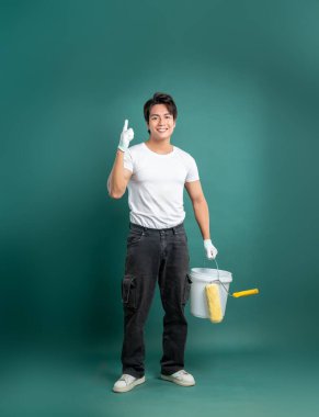 Eldiven takan ve elinde boya kovası tutan neşeli bir ressam, bir gülümseme ile yukarıya doğru işaret ediyor, bu da yüzeyi bir deniz mavisi zeminine karşı boyamak için işaret ediyor..