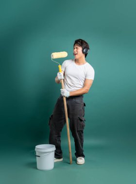 Genç, hevesli bir ressam, elinde boya silindiri, kulaklıkla müzik eşliğinde şarkı söylüyor. Beyaz gömlek ve iş pantolonu giyiyor, boya kovasının yanında duruyor..