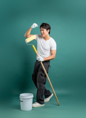 Geniş sırıtışlı bir ressam, sağlam bir deniz mavisi arkaplanına karşı çalışırken boya silindiri tutmasını kutluyor. Çekim, bir projeyi bitirmenin heyecanını gösteriyor..