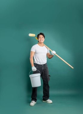 Stüdyoda gülümseyen bir ressam, elinde boya kovası ve evi yenilemek için omzunda boya silindiri olan bir deniz mavisi zeminine karşı sahne alır..