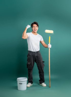 İş kıyafetleri içinde neşeli bir ressam elinde boya silindiri ile duruyor ve görevlerine başlamaya hazır, sağlam bir zemin hazırlıyor, resim yapmak için heyecan veriyor..