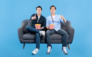İki genç adam gri bir kanepede oturuyorlar, ellerinde patlamış mısır kovaları, ve başparmaklarını kaldırıyorlar. Mavi arka planlı bir film gecesinin tadını çıkarıyorlar.. 