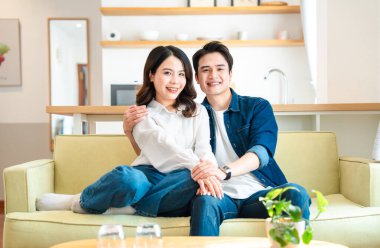 Neşeli bir çift evlerindeki kanepede oturmuş gülümsüyor ve birlikte rahatlıyor.