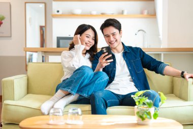 Gülümseyen genç bir çift kapalı bir koltukta rahatlar ve cep telefonunun keyfini çıkarırlar.