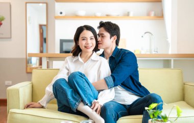 Evde dinlenen genç bir çiftin samimi bir sahnesi Kanepeye oturup gülümsüyorlar