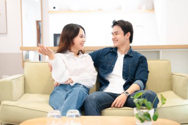 Mutlu bir Asyalı çift açık yeşil bir kanepede dinlenirken keyifli bir sohbetten hoşlanır.