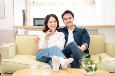 Genç bir çift oturma odasındaki kanepede uzanıp uzaktan kumandayla televizyon seyrediyor.