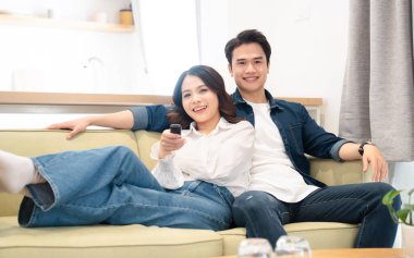 Mutlu bir çift kanepede dinleniyor ve ışık dolu oturma odalarında televizyon seyrediyor.