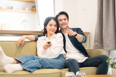 Gülümseyen genç bir çift yeşil bir kanepede dinlenir oturma odasında ekranı gösterir.