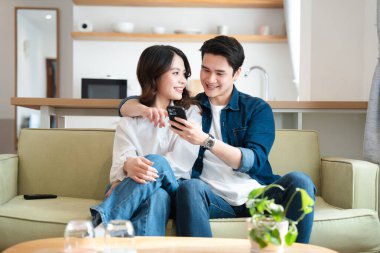 Mutlu bir çift, parlak bir yaşam alanındaki bir koltukta telefona bakarken aynı gülümsemeyi paylaşır.