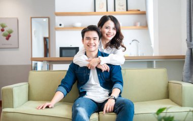 Mutlu genç bir çift modern evlerinde açık yeşil bir kanepede kucaklaşır. Gülümser ve neşe saçar.