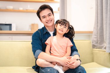 Bir baba ve kızı sıcak bir evde, sıcak bir anın tadını çıkarırken kanepede otururken gülümsüyor.