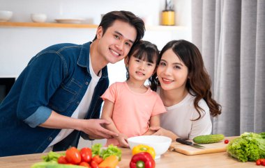 Üç kişilik neşeli bir aile parlak bir mutfakta renkli ve sağlıklı bir yemek hazırlamaya hazır.