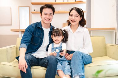 Üç kişilik mutlu bir aile, açık yeşil bir kanepede oturur. Parlak, rahat bir oturma odasında, içten bir gülümsemeyle.