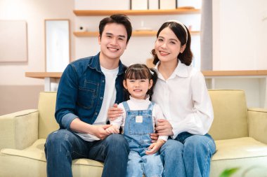 Üç kişilik gülümseyen bir aile sıcak bir kanepeye oturmuş sevgi ve mutluluk yayıyorlar.