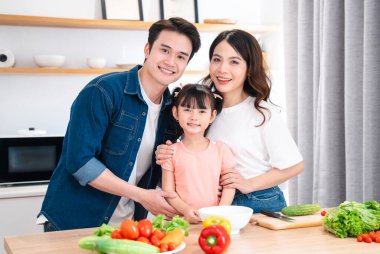 Mutlu bir aile, parlak mutfağında renkli sebzelerle sağlıklı bir yemek hazırlamaya hazır bir şekilde gülümsüyor.