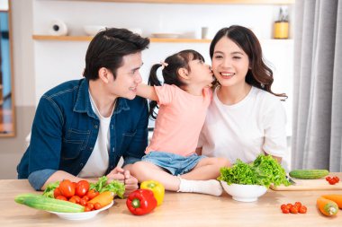 Anne, baba ve küçük kızı da dahil olmak üzere bir aile mutfakta sebzelerle eğleniyor.