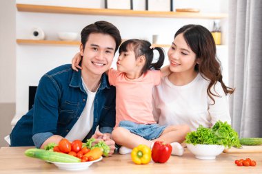 Gülümseyen bir anne baba ve çocuk evde sağlıklı bir yemek için taze sebzeleri birlikte hazırlıyorlar.