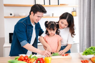 Mutfaktaki bir aile sağlıklı bir yemek için kızlarının taze sebze kesmesine yardım ediyor.