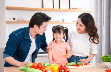 Bir aile mutfakta yemek hazırlıyor. Küçük kız sebze tutuyor ve gülümsüyor.