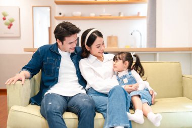 Üç kişilik bir aile oturma odasındaki bir kanepede oturup birbirlerine mutlu bir şekilde bakıyorlar.