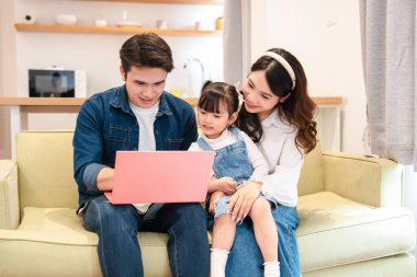 Üç kişilik gülümseyen bir aile oturma odasındaki dizüstü bilgisayara bakarken koltukta oturuyor.