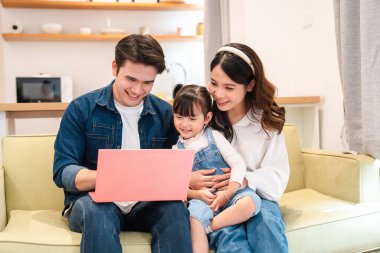 Evlerinde pembe bir dizüstü bilgisayara bakarken koltukta oturan mutlu bir aile.