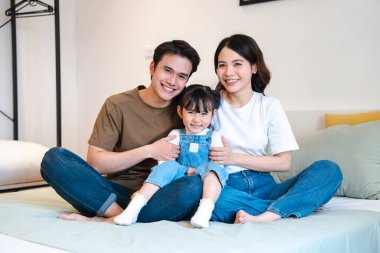 Mutlu bir Asyalı aile anne ve babadan oluşuyor. Baba ve kız gülümsüyor ve yatakta birlikte oturuyorlar.
