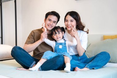 Mutlu bir anne baba ve kızı kot pantolon giyerken yatakta bacak bacak üstüne atarak otururlar.