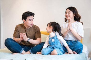 Üç kişilik gülümseyen bir aile bir yatakta oturmuş arkadaşlıklarının tadını çıkarıyor ve eğleniyorlar.