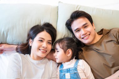 Neşeli bir Asyalı aile tarafsız bir yatakta uzanmış birlikte güzel vakit geçiriyorlar.