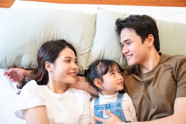 Mutluluk saçan bir yatakta uzanan bir aile ile göz göze gelen bir aşk gülümsemesi arasındaki sıcak bir an.