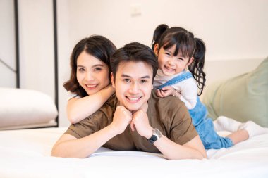 Üç kişilik bir aile bir yatakta gülümser ebeveynlerin sevgisi ve çocuğun neşesi kucaklaşmada görülür.