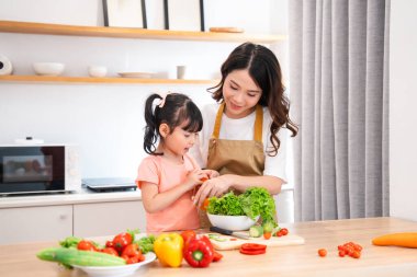 Parlak bir mutfakta bir anne ve kız taze sebzeler hazırlar. Yemek pişirerek özel bir bağ kurarlar.