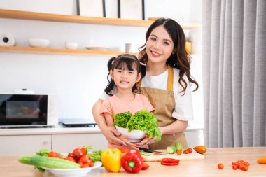 Gülümseyen anne ve kızı, modern mutfaklarında birlikte sağlıklı bir salata hazırlıyorlar.
