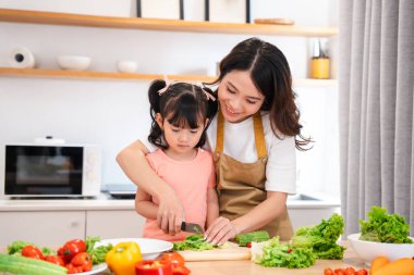 Bir anne ve kız birlikte salata hazırlıyorlar. Parlak bir mutfakta yemek pişirmeyi öğretiyorlar.