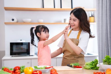 Asyalı anne ve kızı mutlu mesut bir şekilde bir mutfakta beşlik çakıyor ve birlikte sağlıklı sebzeler hazırlıyorlar.