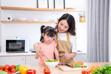 Anne ve kızı mutfakta taze salata malzemelerini karıştırıyorlar. Bu bir aile bağı anı.